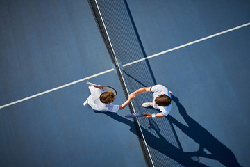 Overhead view young male tennis players handshaking at net on sunny blue tennis court
