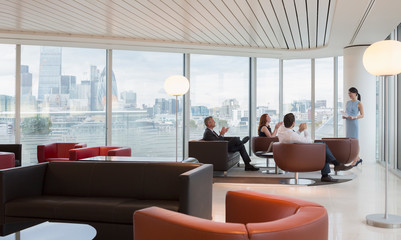 Business people clapping for businesswoman leading meeting in highrise urban lounge