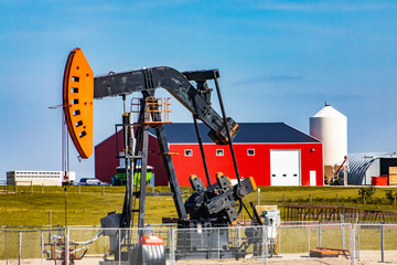 A oil well pumpjack, overground reciprocating pump, is seen by a large ranch in Alberta. With grain...