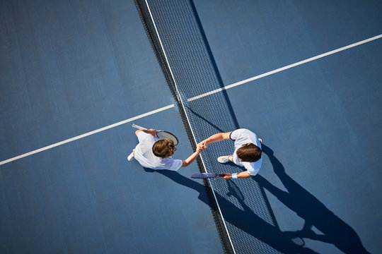 Overhead view young male tennis players handshaking at net on sunny blue tennis court