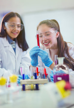 Smiling girl students examining liquid in test tube, conducting scientific experiment in laboratory classroom