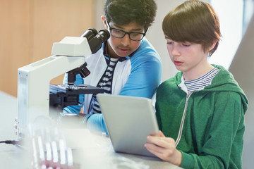 Focused boy students using digital tablet at microscope in laboratory classroom