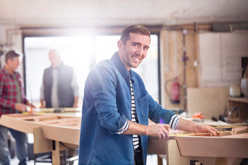 Portrait smiling male carpenter measuring wood on boat in workshop