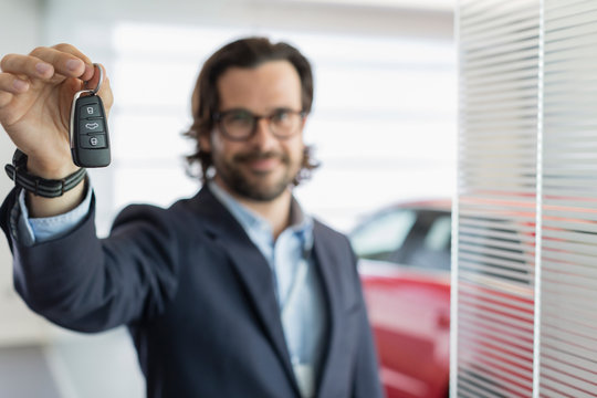 Portrait confident car salesman holding, showing car key in car dealership showroom