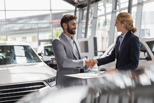 Car saleswoman male customer handshaking in car dealership showroom