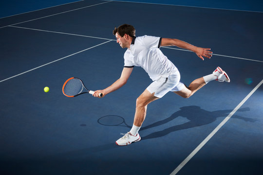 Male tennis player playing tennis, reaching tennis racket on tennis court