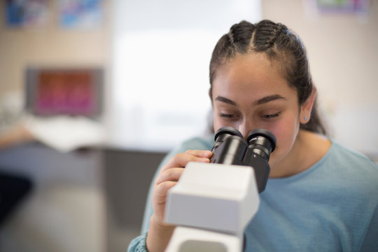 Girl student using microscope in classroom - Powered by Adobe