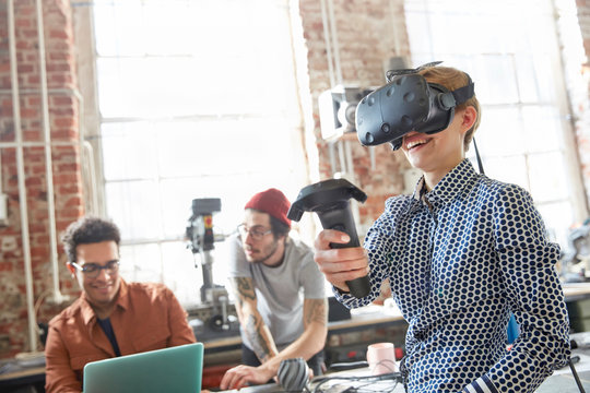 Female designer texting virtual reality simulator glasses using joystick in workshop
