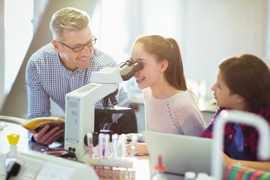 Male teacher helping girl student using microscope, conducting scientific experiment in laboratory classroom