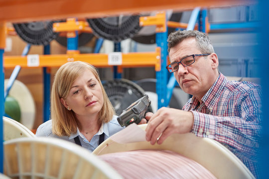 Male female supervisors using IR code scanner, scanning spool in fiber optic warehouse