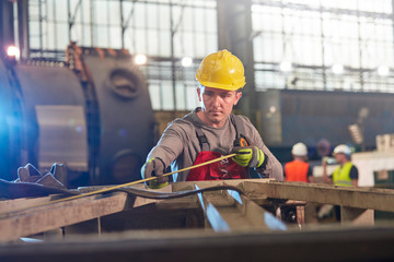 Male worker with tape measure measuring steel in factory