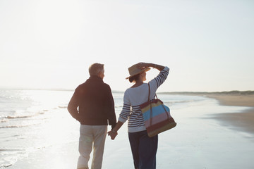 Affectionate mature couple holding hands and walking on sunny beach