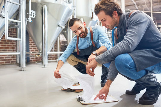 Male brewers with clipboard near vat in brewery