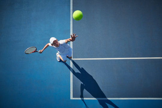 Overhead view of young male tennis player playing tennis, serving the ball on sunny blue tennis court