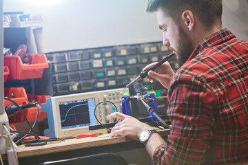 Male engineer assembling electronics, using soldering iron