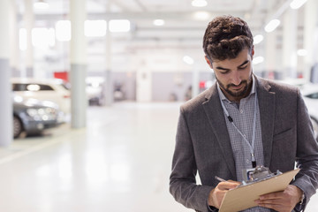 Car salesman writing on clipboard in car dealership auto repair shop