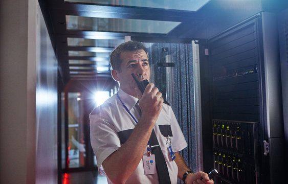 Male security guard using walkie-talkie in dark server room