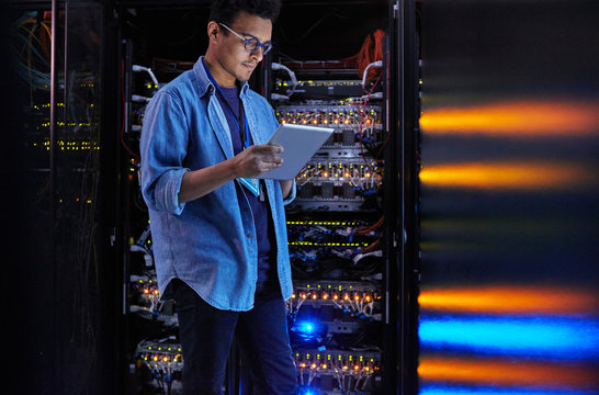 Focused male IT technician using digital tablet at panel in dark server room - Powered by Adobe