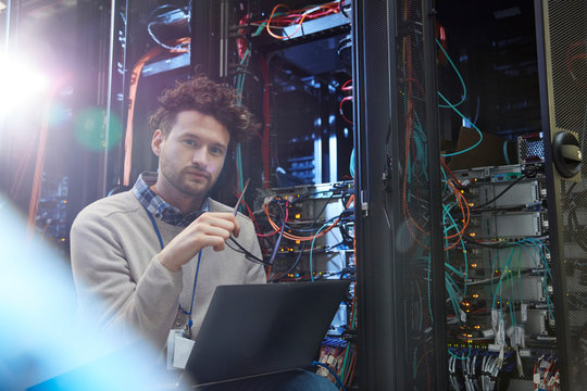 Portrait confident male IT technician working at laptop in server room