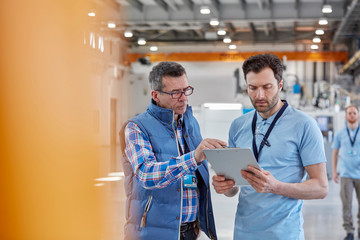 Male worker and supervisor with clipboard talking in factory