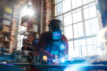 Welder welding with welding mask and torch in workshop