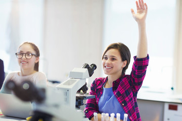 Smiling girl student asking a question behind microscope in classroom laboratory
