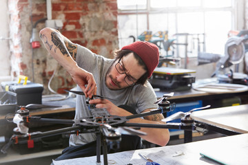 Male designer with tattoos assembling drone in workshop