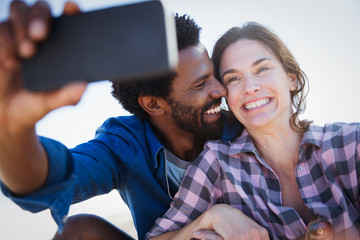 Smiling, enthusiastic multi-ethnic couple taking selfie camera phone