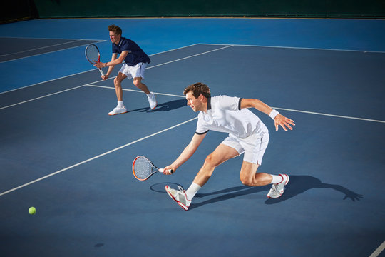 Young male tennis doubles players playing tennis, reaching tennis racket on blue tennis court