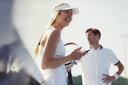 Laughing female tennis player holding cell phone and tennis racket