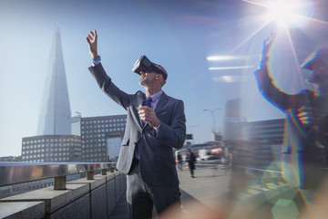 Businessman using virtual reality simulator glasses, reaching for sky on sunny urban bridge, London, UK