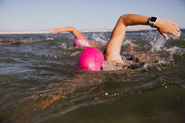 Female open water swimmer with smart watch swimming in sunny ocean