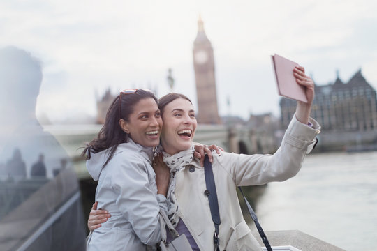 Enthusiastic, smiling women friend tourists taking selfie digital tablet camera near Big Ben, London, UK