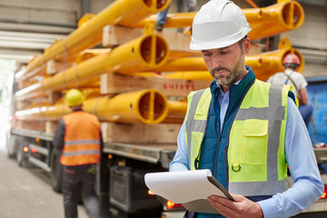 Male foreman reading paperwork on clipboard in factory
