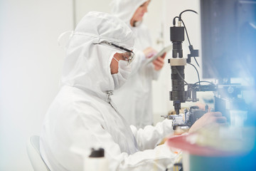 Workers in protective suits using machinery in fiber optics research testing laboratory