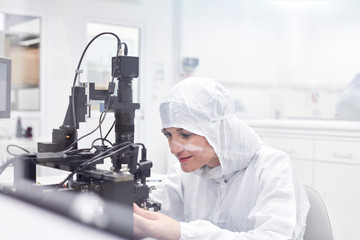 Female engineer in clean suit using equipment in fiber optics research testing laboratory