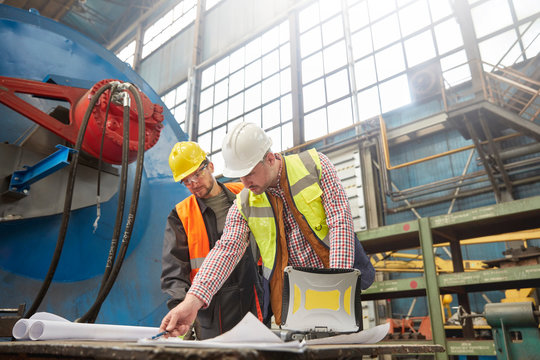 Male foreman and engineer reviewing blueprints in factory