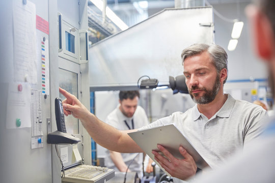 Male supervisor clipboard using machinery control panel in factory