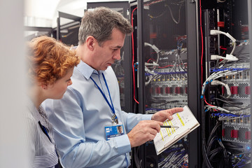 IT technicians with clipboard examining panel in server room