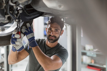 Portrait confident male auto mechanic working under car in auto repair shop