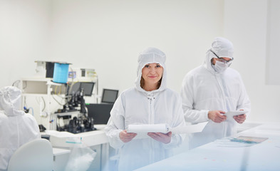 Portrait smiling female engineer in protective suit paperwork in fiber optics research testing laboratory