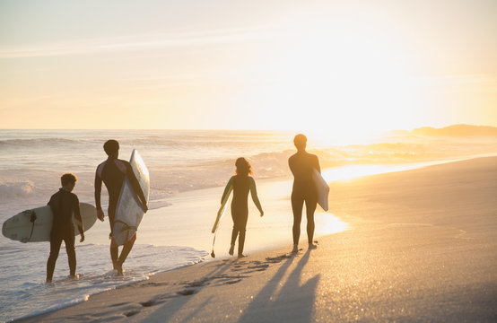 Family Surfers Walking With Surfboards On Sunny Summer Sunset Beach