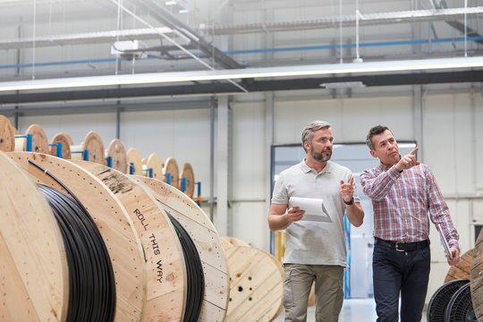 Male supervisor worker clipboard walking along spools in fiber optics factory