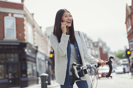 Smiling young woman commuting on bicycle, talking on cell phone on sunny urban street