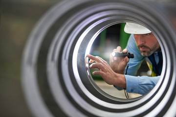 Male engineer with flashlight inspecting steel cylinder