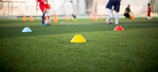 Marker Cone on green artificial turf with blurry kid soccer players are training background. Soccer academy.