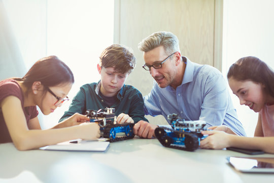 Male teacher helping students assembling robotics in classroom
