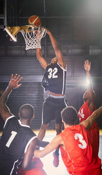 Young male basketball player dunking the ball into hoop defenders below