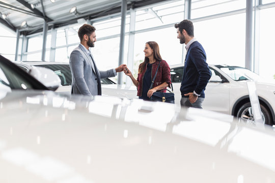 Car salesman giving car keys to customers in car dealership showroom