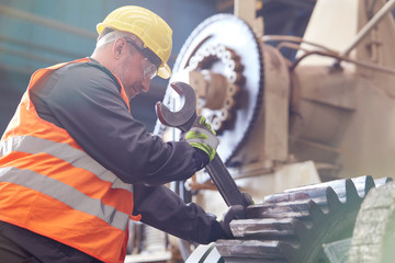 Male worker using large wrench on cog in factory
